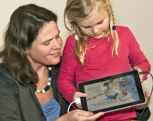 Hier ziet u de iPad met het witte verloopkabeltje en de geluidskabel. Het meisje bedient de iPad, de zaal kijkt mee op een groot scherm.